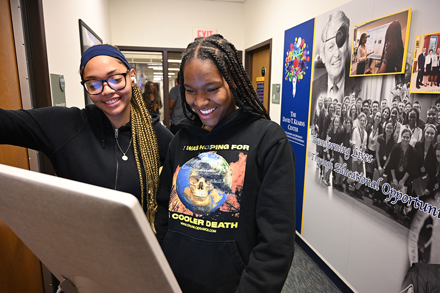 Two students smile as they use a kiosk to sign in.