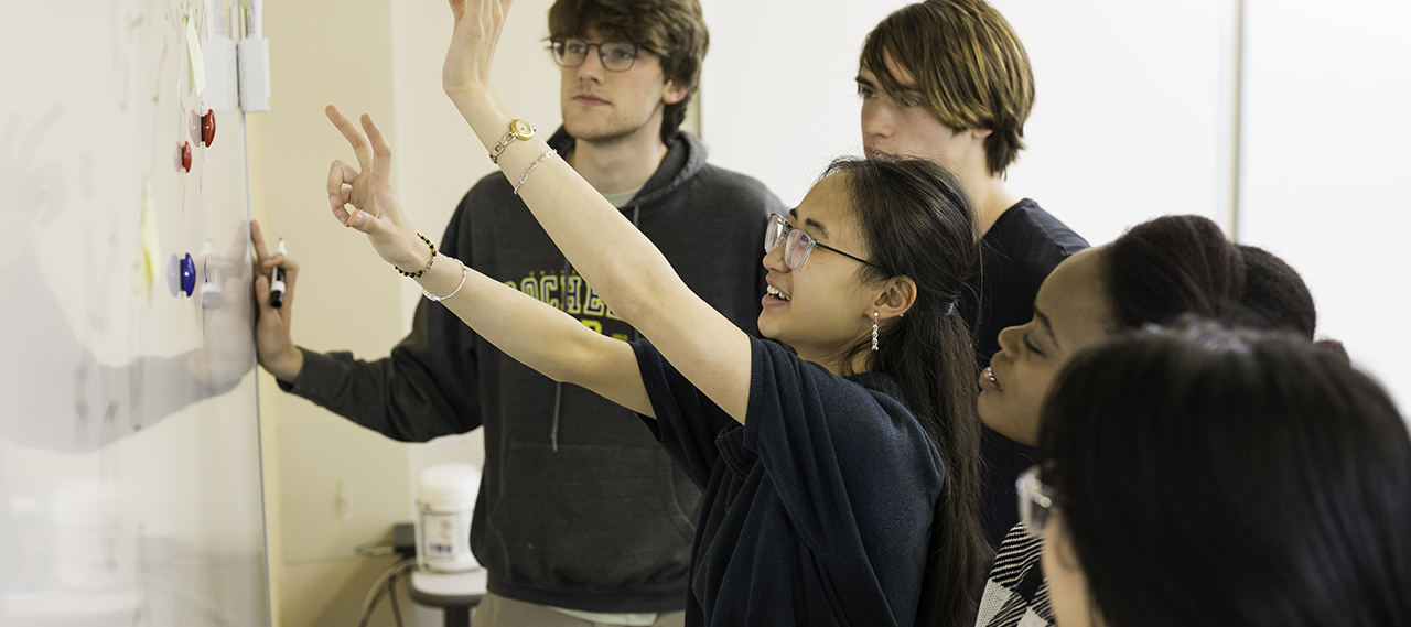 A group of five students working at a white board.