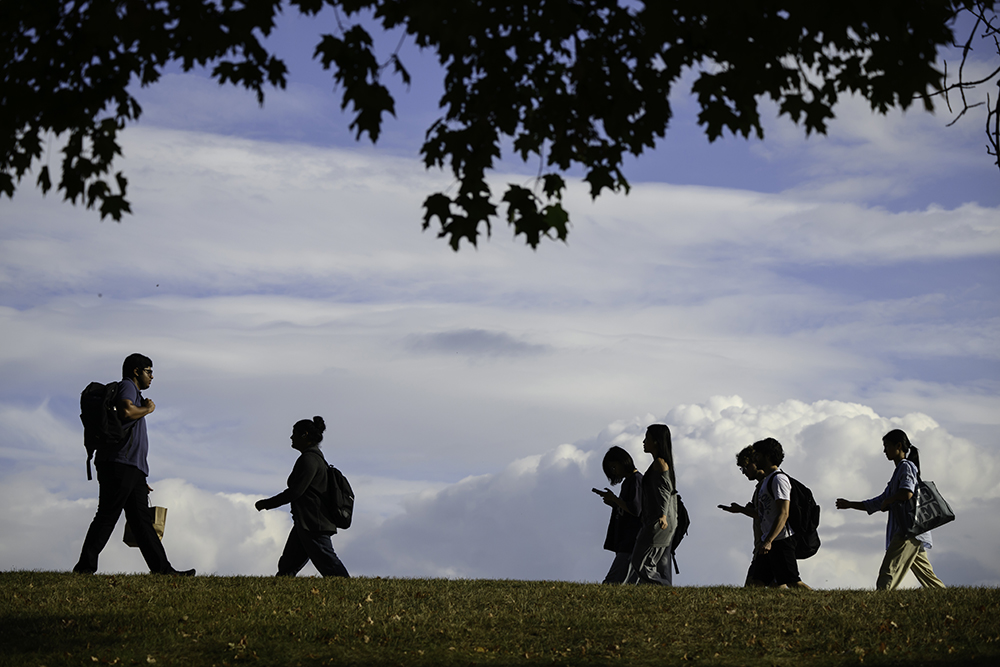 Students walking across a horizon with puffy white clouds behind them.