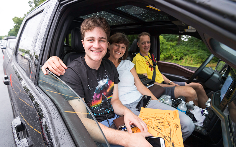 Photo of a student and their parents posing for the camera inside their vehicle