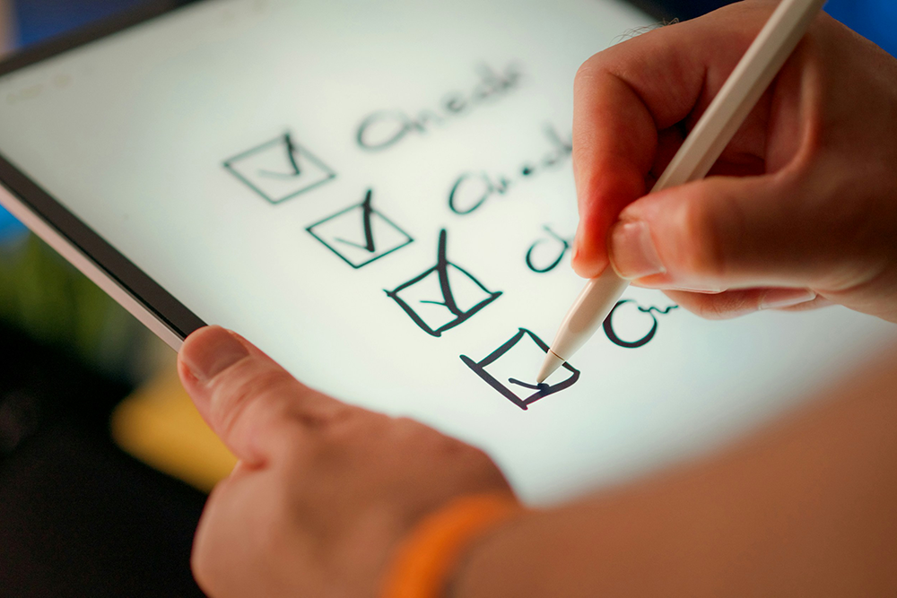 A hand with a stylus hovers over a digital checklist on a tablet