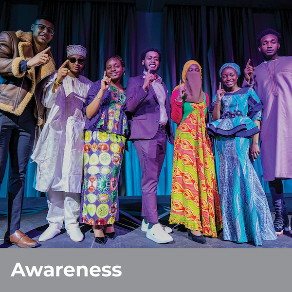 Awareness - Group of students in colorful, assorted garb with their index fingers extended