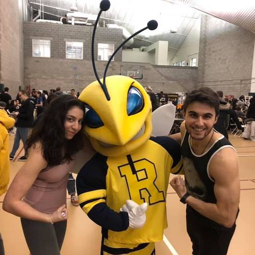 Two students flexing their biceps next to the Rocky mascot