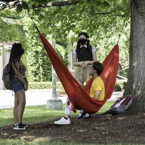 Two students outside while one lounges in a hammock