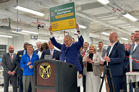 Senator Chuck Schumer hoists a "NY Semiconductor Superhighway" while speaking at a lectern at MCC.