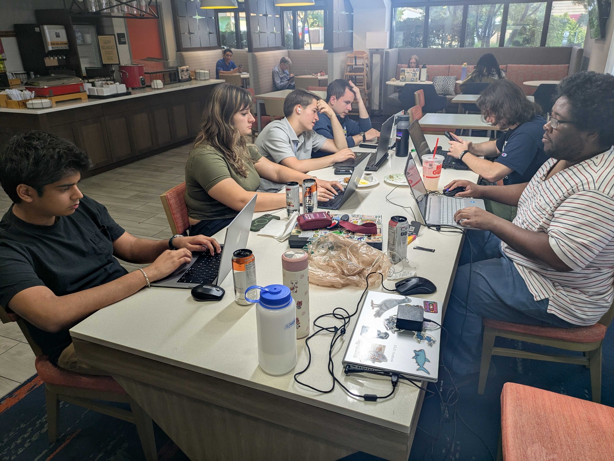 A group of people sitting around a table in a coffee shop while working on their laptops.