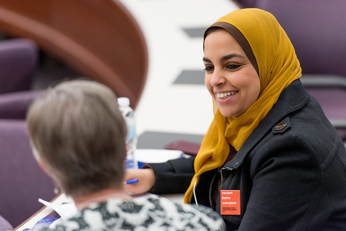 Woman wearing hijab and a button that reads RACISM HURTS EVERYONE speaks to another woman at a conference