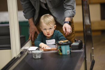 A toddler in front of a toy cashier conveyor belt