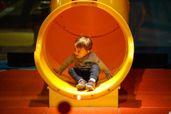 A candid photo of an excited male toddler at the bottom of a slide at the George Eastman Circle Family Celebration, held on April 27, 2023 within Rochester New York.
