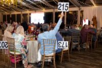 man raises number 215 from seat at table for auction