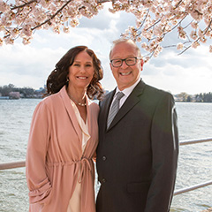 Douglas and Sharon Dompkowski under cherry blossoms and a body of water behind them