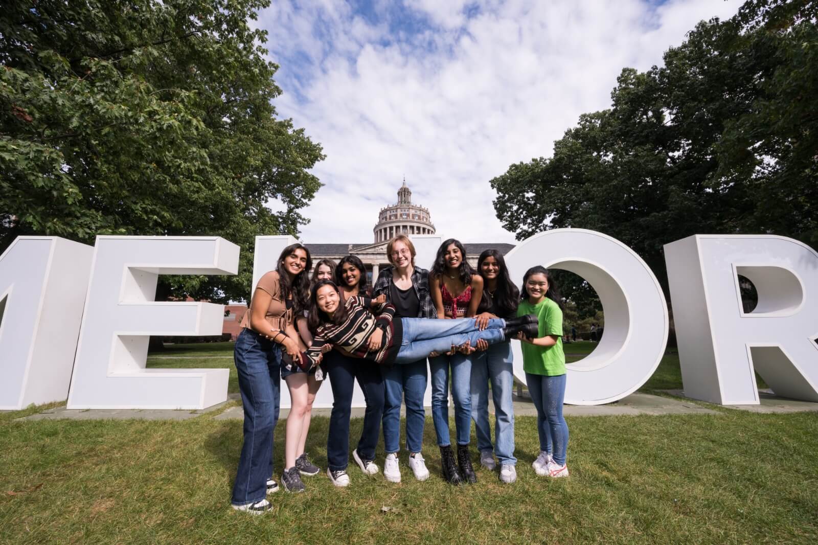 A group of seven young women posing in front of large block letters spelling out 