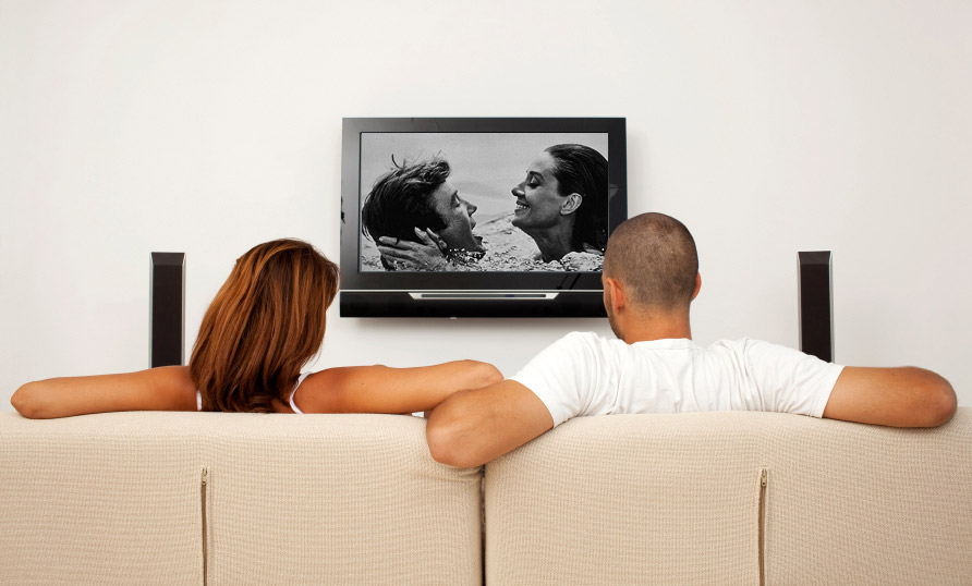 woman and man sit on couch watching a movie.