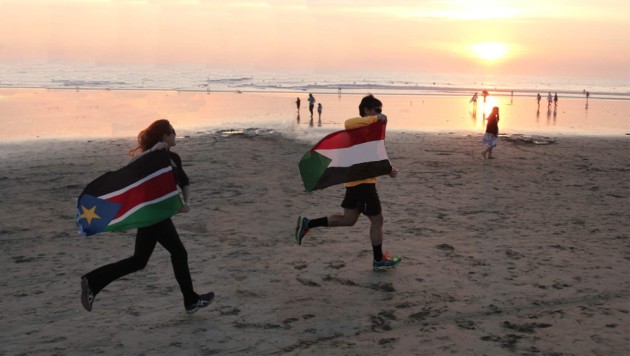 people carrying flags, running on a beach
