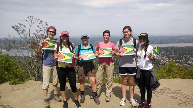 women on a mountain top, holding Guyana's flag