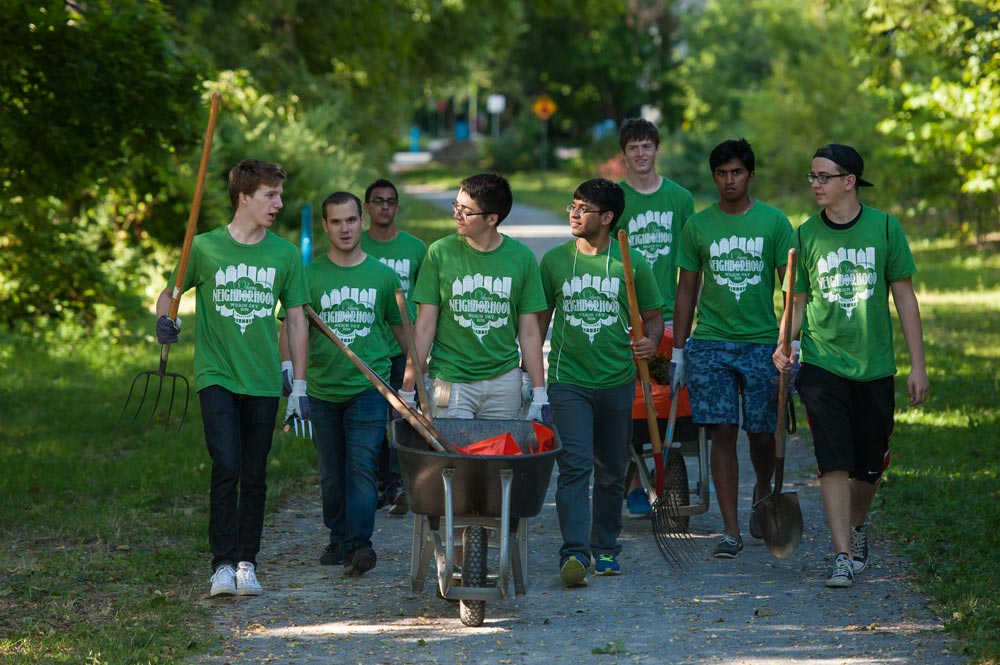 large group of students in matching t-shirts pushing wheelbarrows and carrying gardening equipment