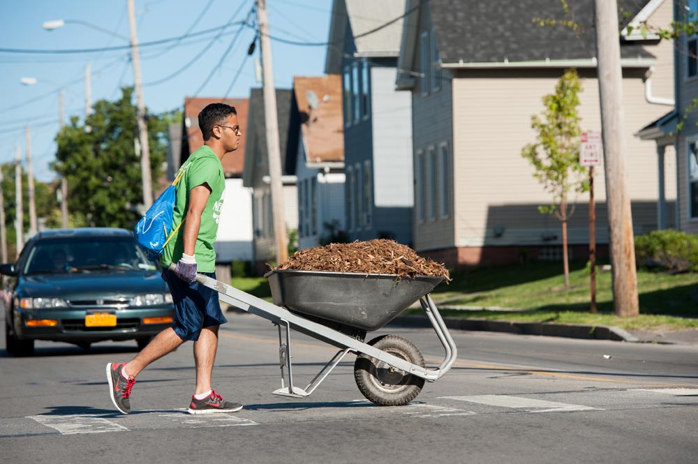 student pushing a wheelbarrow across a street