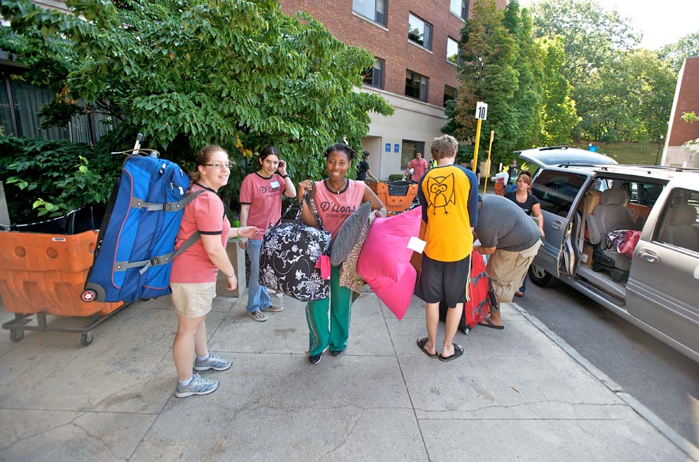 group of student helpers in matching t-shirts carrying pillows, suitcases