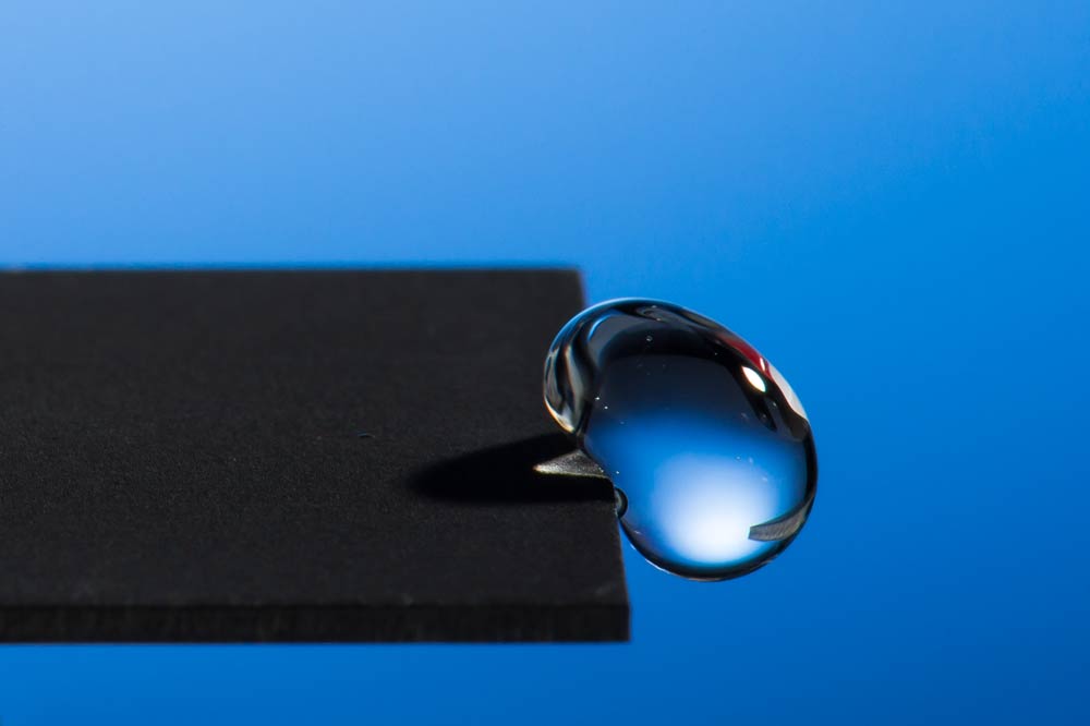 photo of a droplet of liquid hanging off the edge of a surface