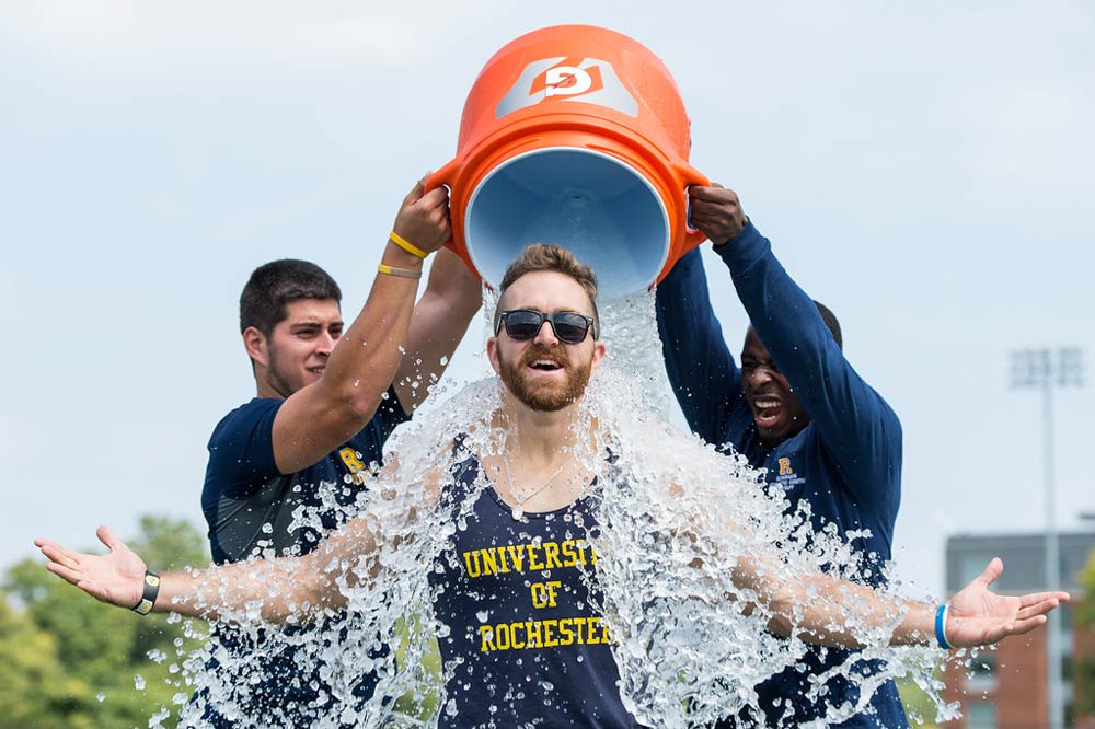 students dumping a bucket of ice over the head of a coach as part of the Ice Bucket Channel
