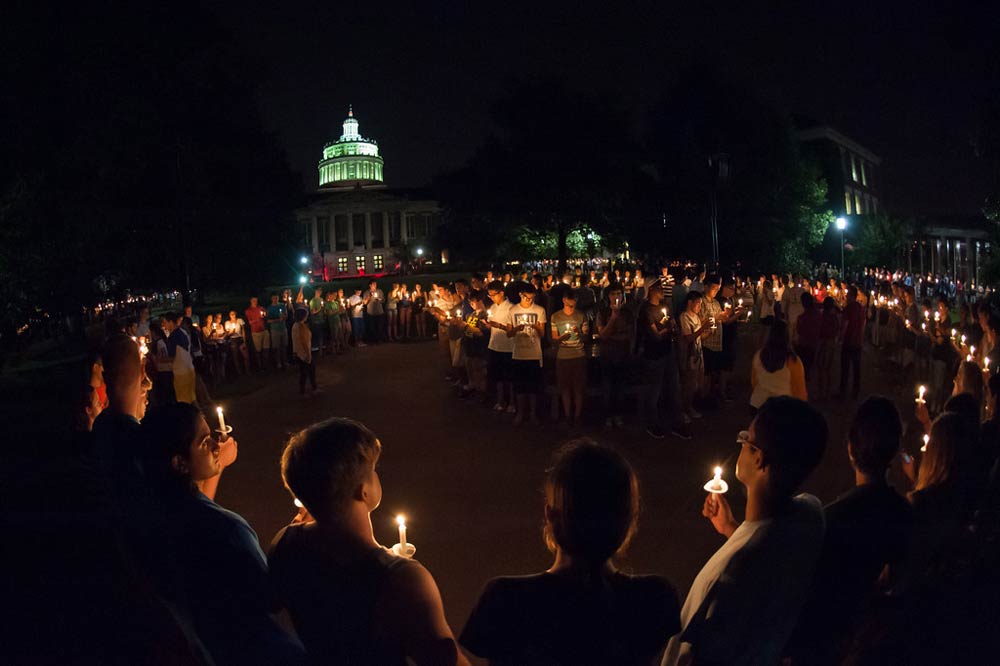 ring of students on the quad at night holding candles in a ceremony