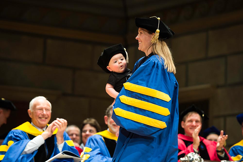 graduate crosses the stage holding a baby