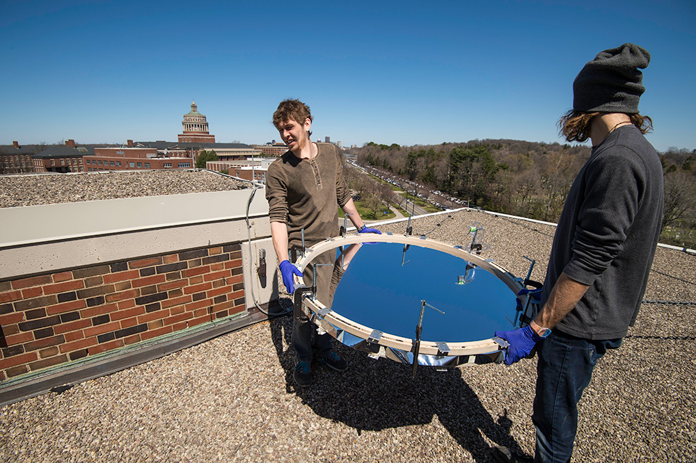 student carry round solar mirror onto roof, library tower in the background