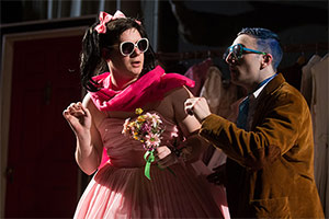 two men onstage, one dressed as a woman wearing sunglasses