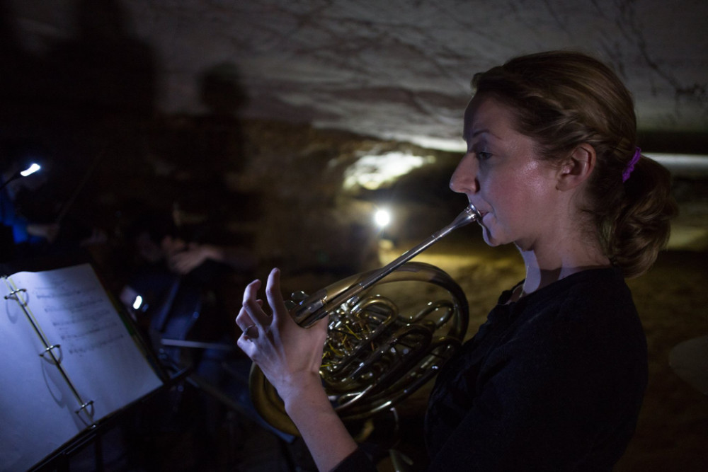Close-up of woman playing French horn inside a national park cave.