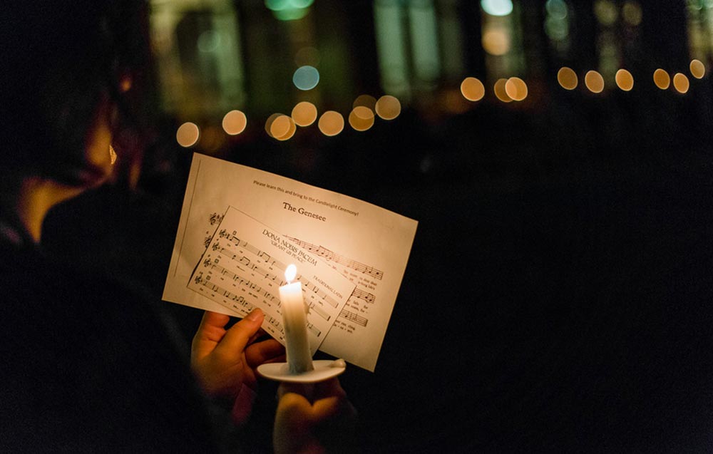 student holding a candle in front of sheet music for THE GENESSEE