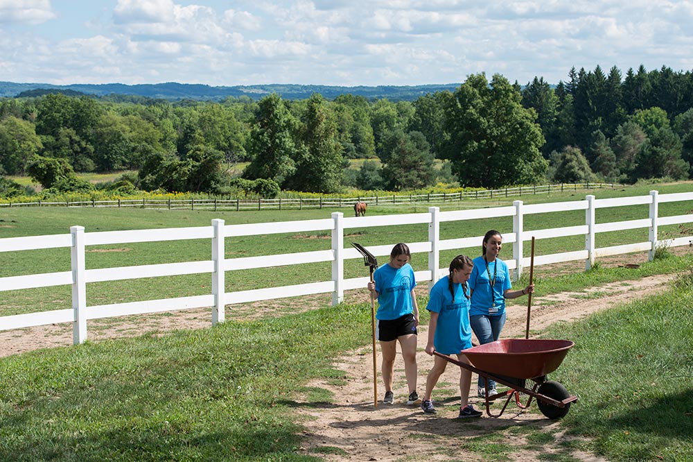 student pushing a wheel barrow, with horses in the backgroun