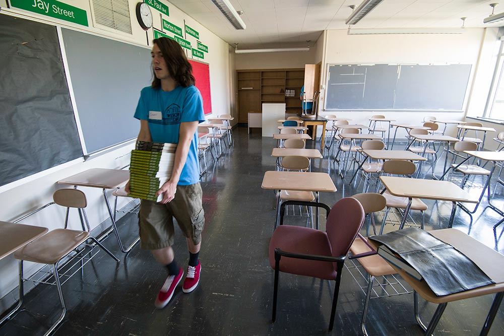 student in empty classroom carrying books