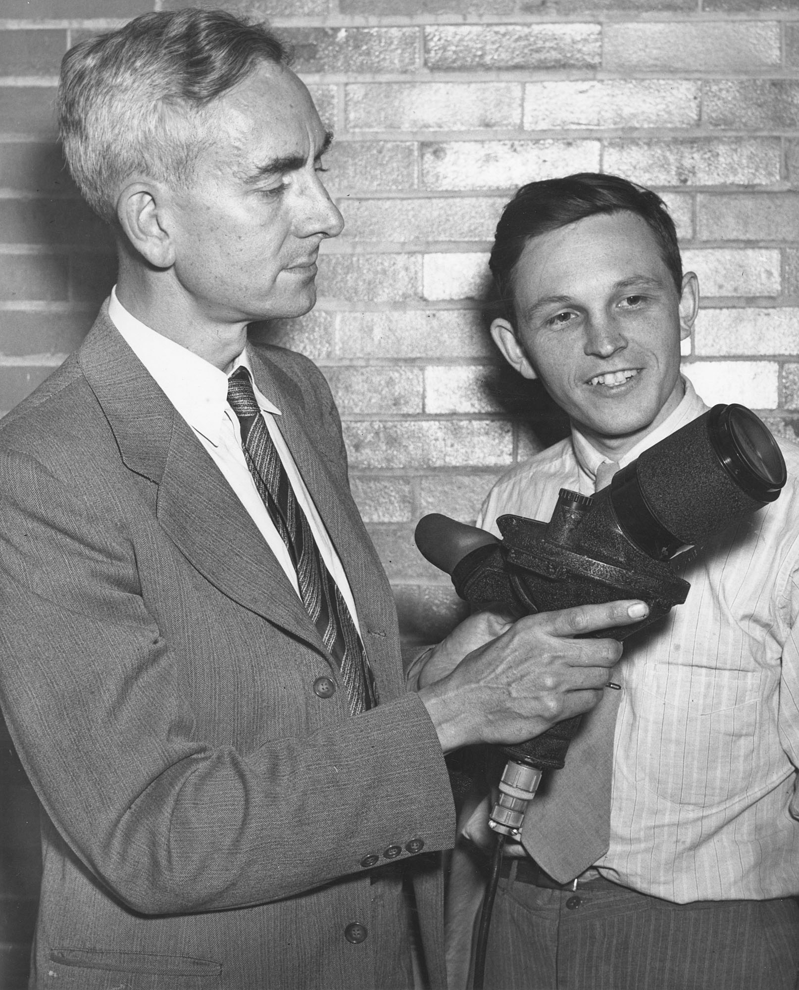 man holding an optical instrument as another man looks on