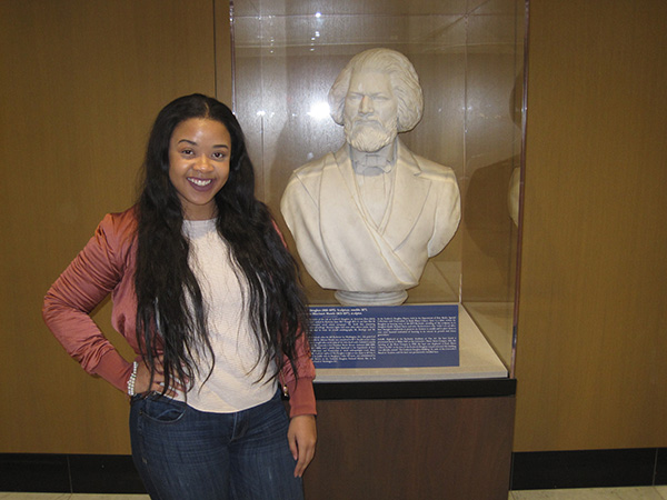 student poses with bust of Frederick Douglass