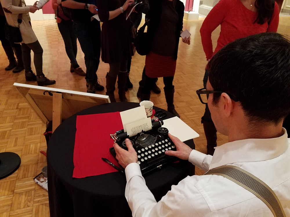 man typing on a vintage typewriter with a crowd of people watching him