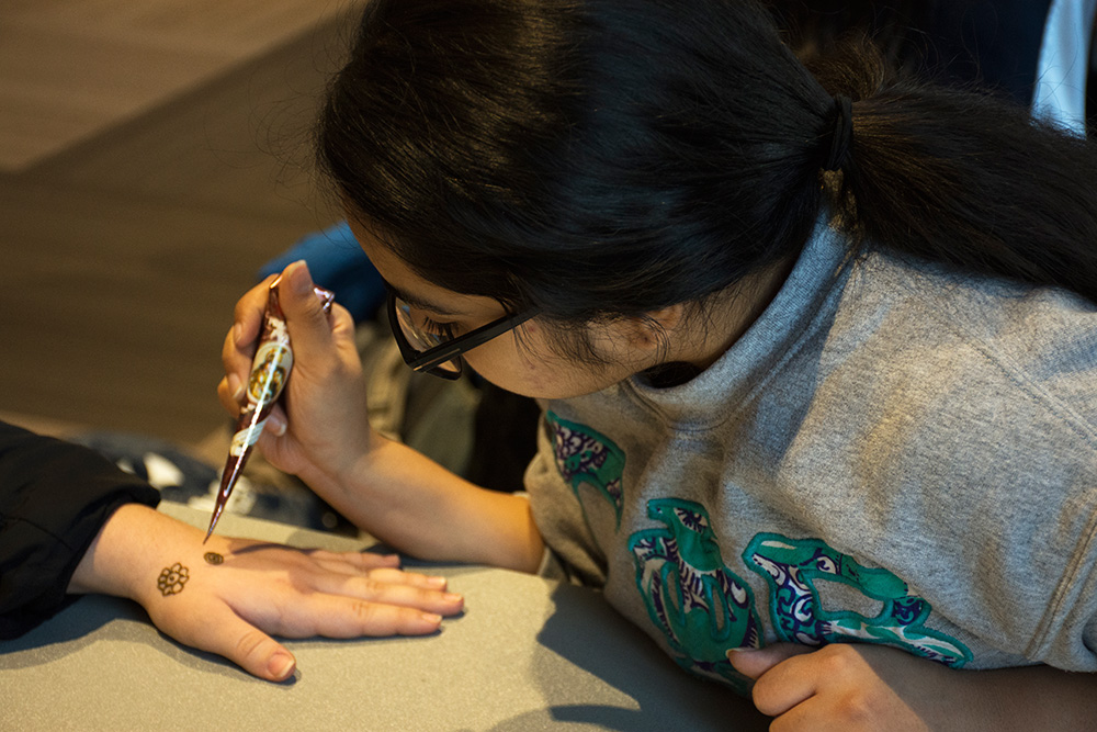 student painting a henna tattoo on someone's hand
