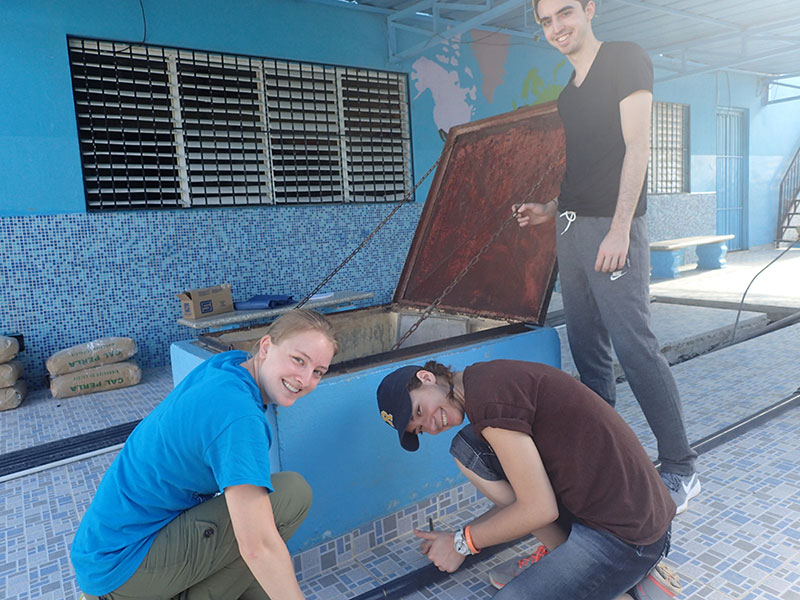 three students looking at water filtration system in brightly painted building