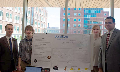 Four students standing by VocalEyes poster