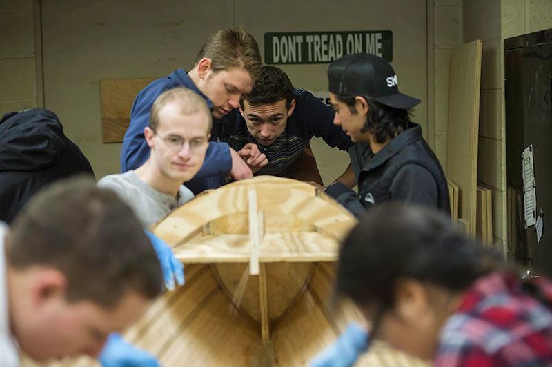 students surrounding a wooden boat, looking to make sure it is level