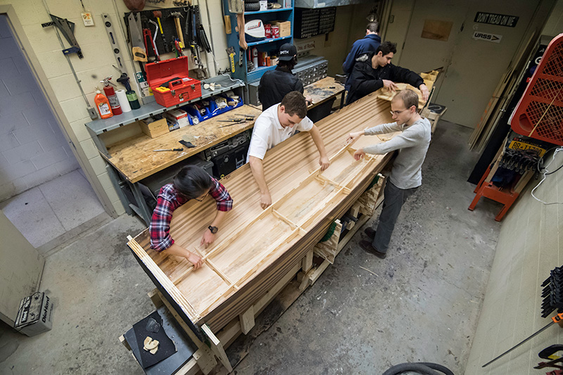 overhead view of students working on a wooden boat