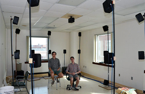 two students in a room surrounded by speakers on poles