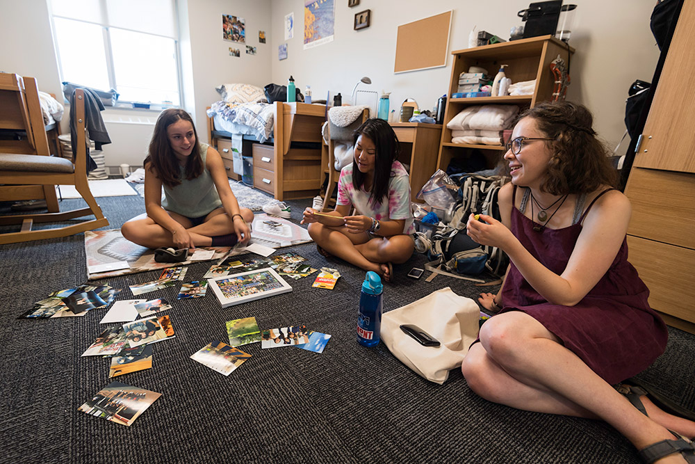 three students sitting on floor, looking at photos