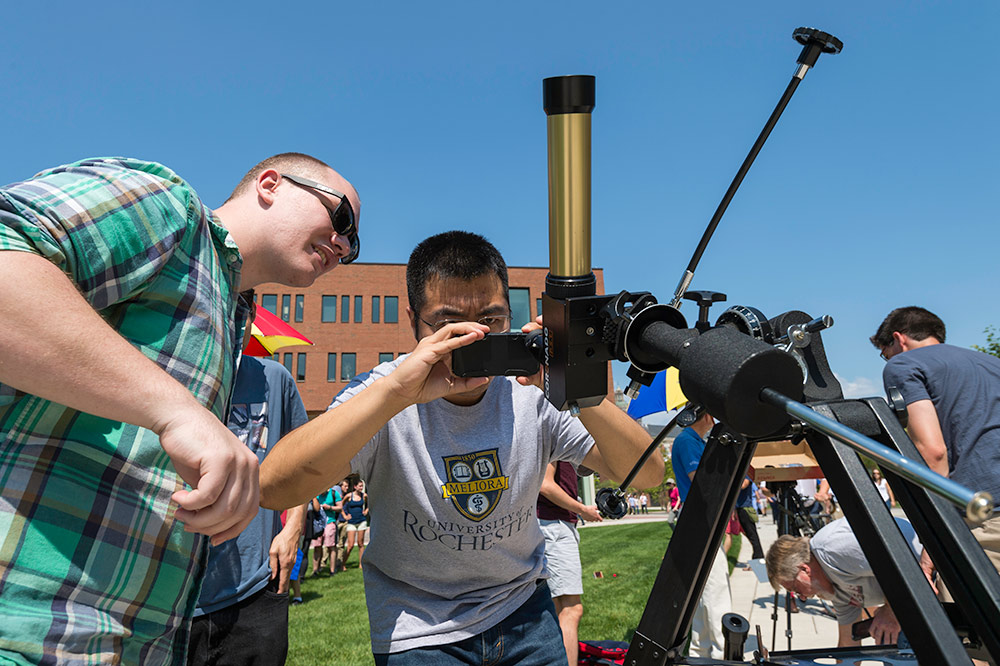 students with smartphones looking through a telescope