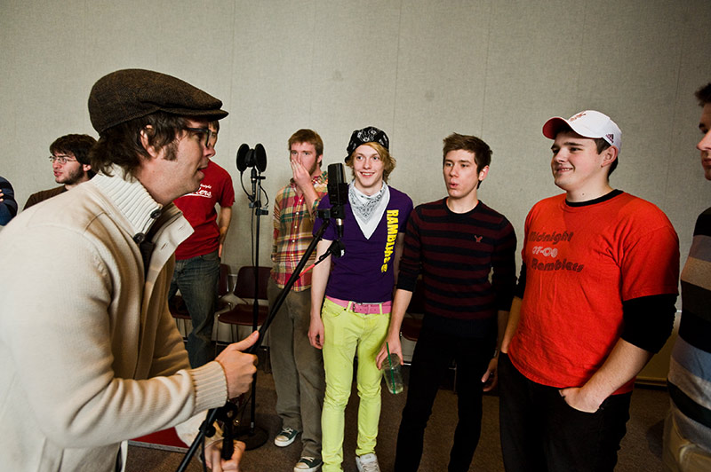 large group of performers standing around a microphone