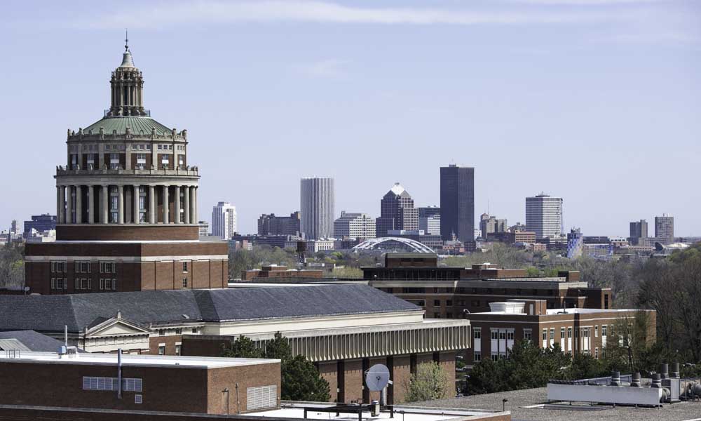 City of Rochester skyline in background with Rush Rhees Library tower and other River Campus buildings in the foreground.