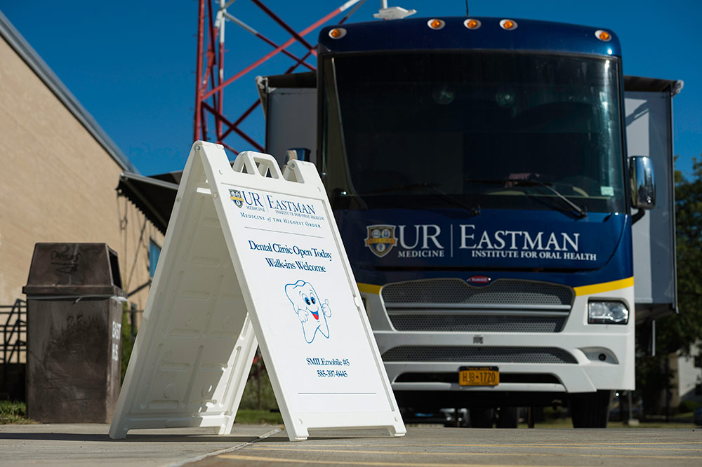 sign for smile mobile and UR Eastman bus outside a school