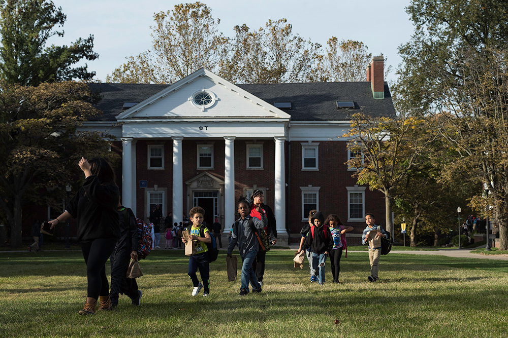 kids with trick or treat bags run across quad