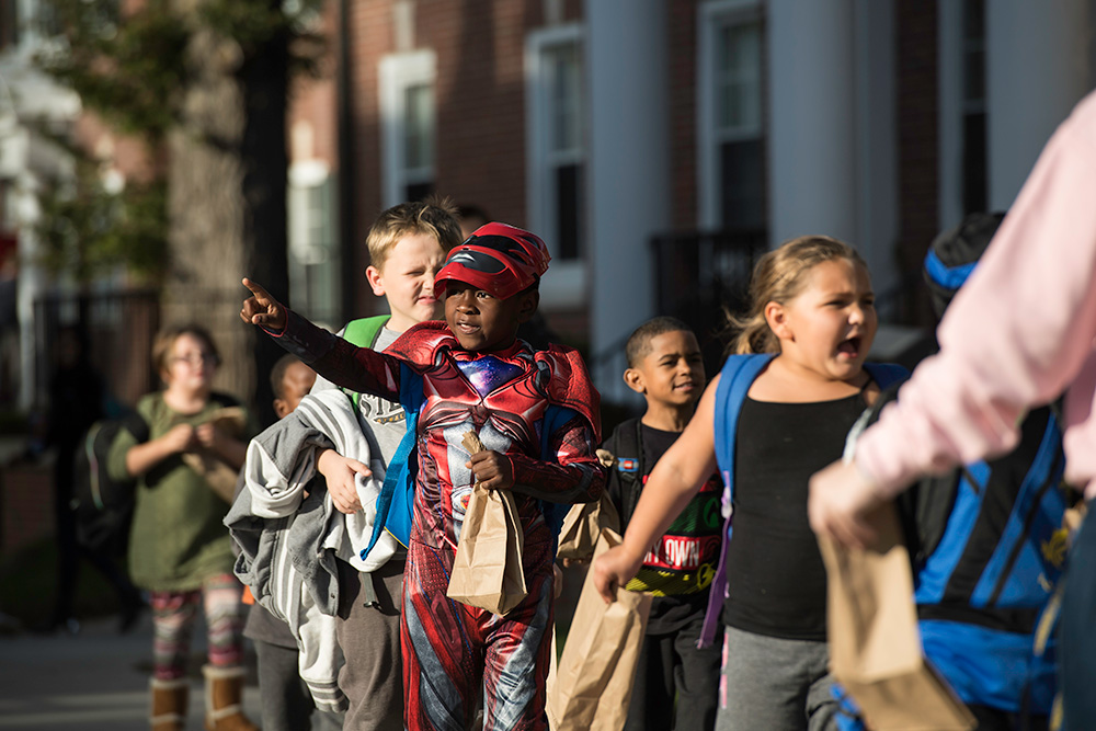 kids in Halloween costumes walk in a line across the quad