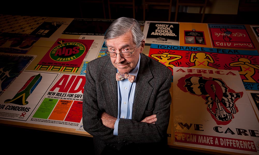 Edward Atwater with arms crossed and AIDS posters laid out on a table behind him.