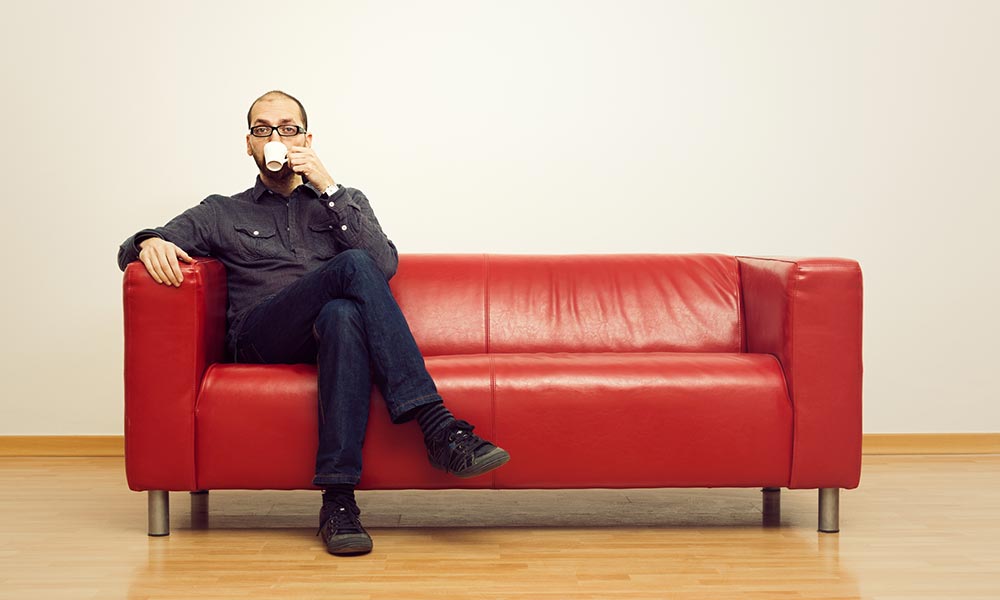 man drinking coffee while seated alone on a sofa
